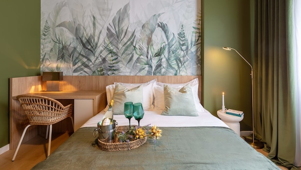 Habitación de hotel con una cama, un escritorio, una silla, una mesita de noche y una pared con estampado de hojas.