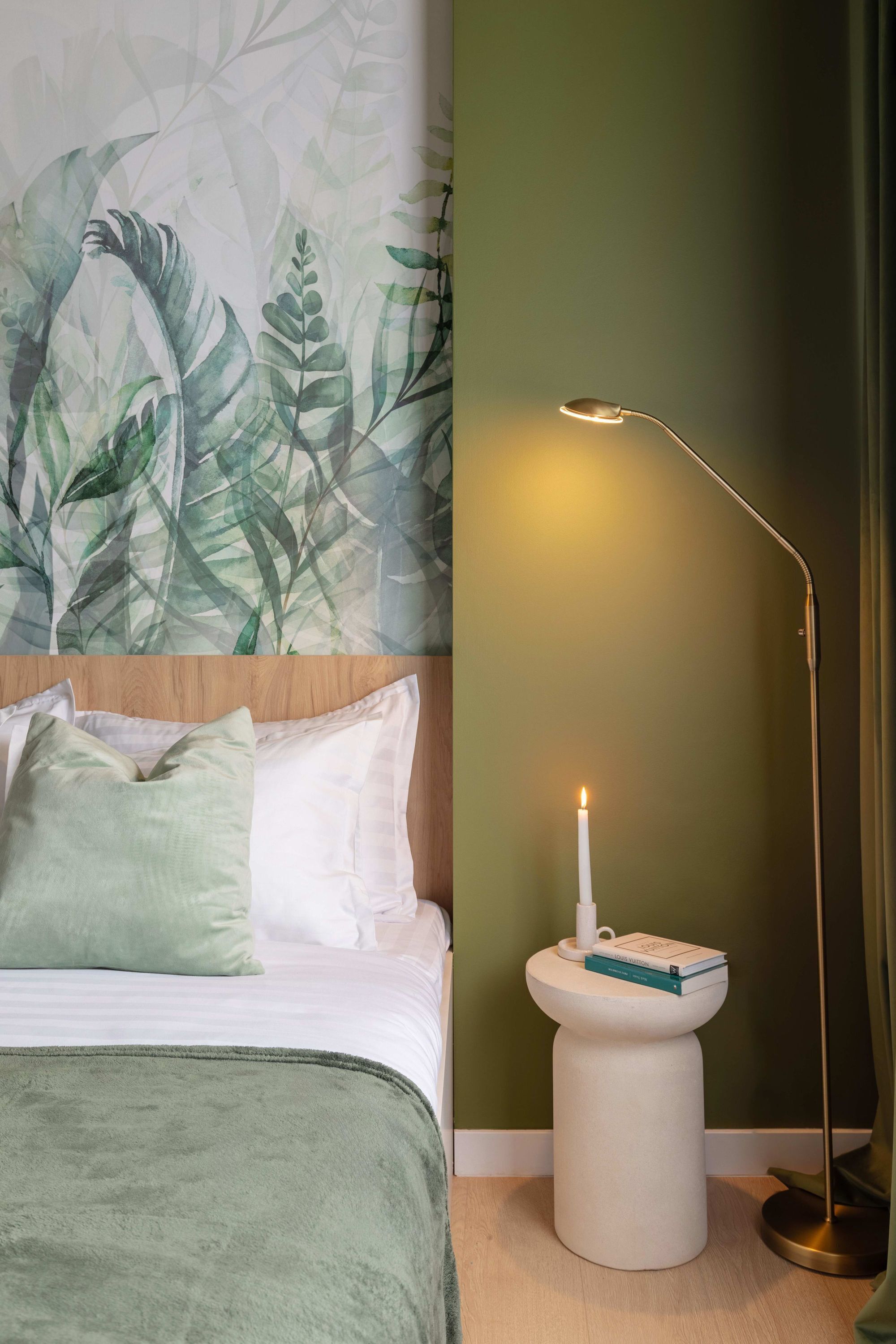 Ein ordentlich gemachtes Bett mit Kissen, ein Nachttisch mit Kerze und eine Stehlampe.