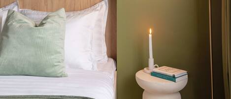 Ein ordentlich gemachtes Bett mit Kissen, ein Nachttisch mit Kerze und eine Stehlampe.