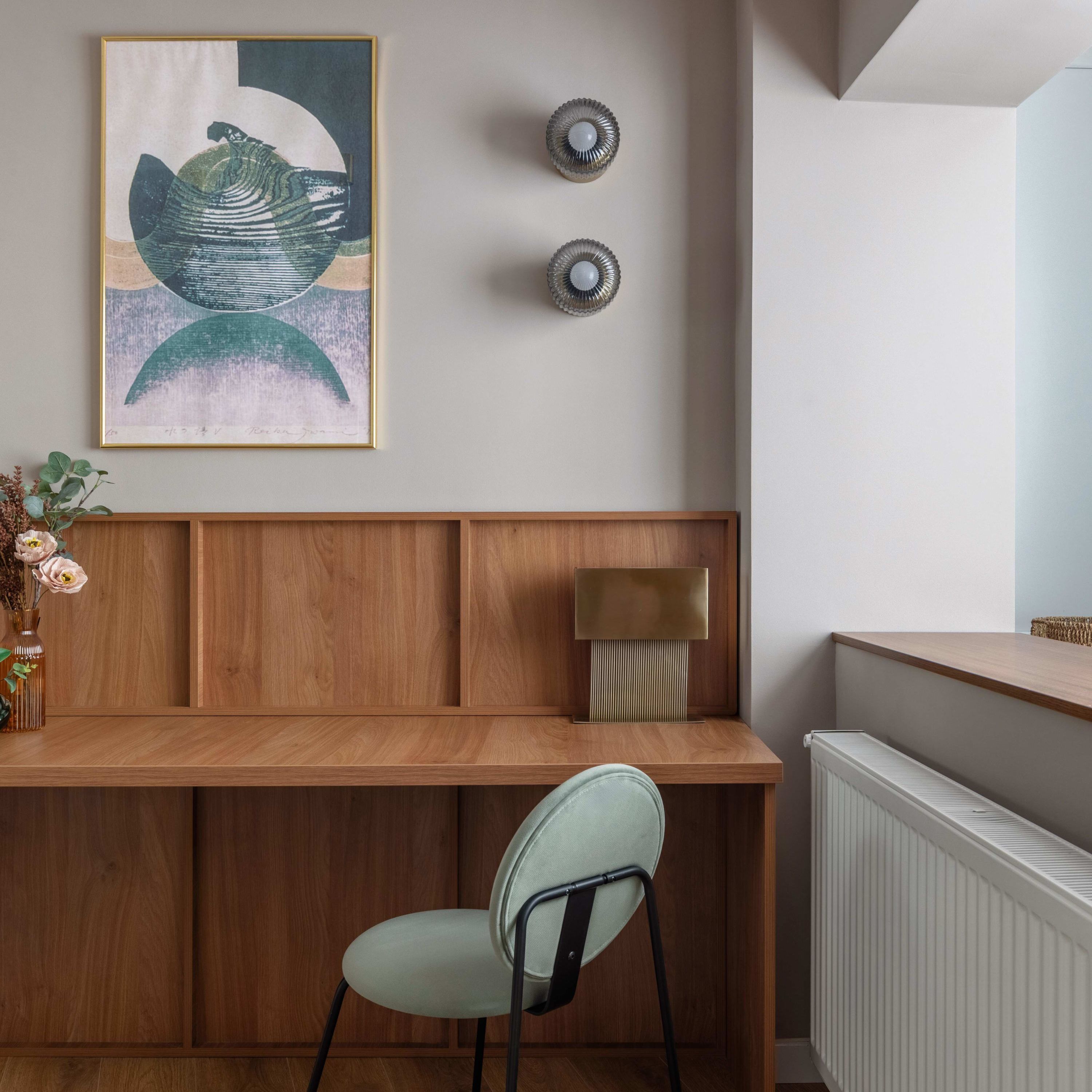 A modern room with a wooden desk, a chair, a radiator, and a wall-mounted lamp.