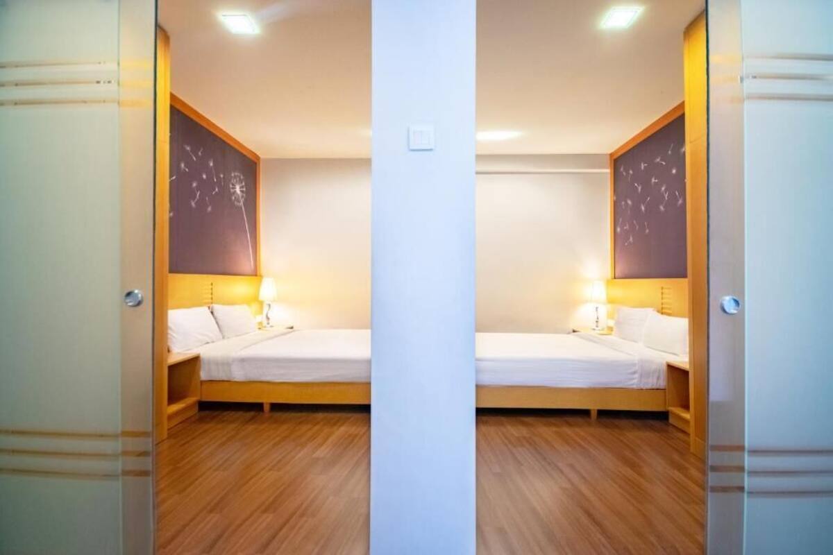 A mirrored room with two beds, wooden flooring, and wall-mounted lamps.