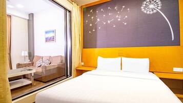 Une chambre d’hôtel avec un lit, un canapé, une petite table, une fenêtre et un mur orné d’une œuvre d’art représentant des pissenlits.