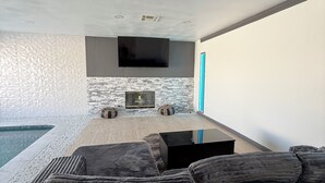 Ein modernes Wohnzimmer mit Kamin aus Stein, einem Flachbildfernseher und einem Pool.