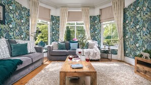 A cozy living room with a grey sofa, a wooden coffee table, and a floral wallpaper.