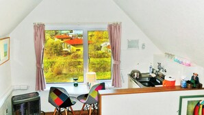 Een kamer met een groot raam, een eethoek met stoelen, een keuken en een kleurrijk glas-in-lood plafond.