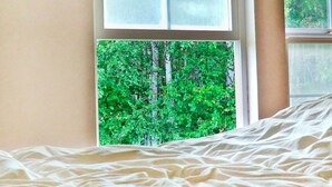 Een bed met uitzicht op een groene boom door een raam.