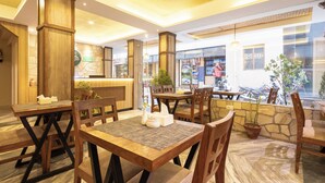 A restaurant with wooden tables and chairs, a stone wall, and a view of the street outside. - Divya Boutique Inn (Kathmandu)