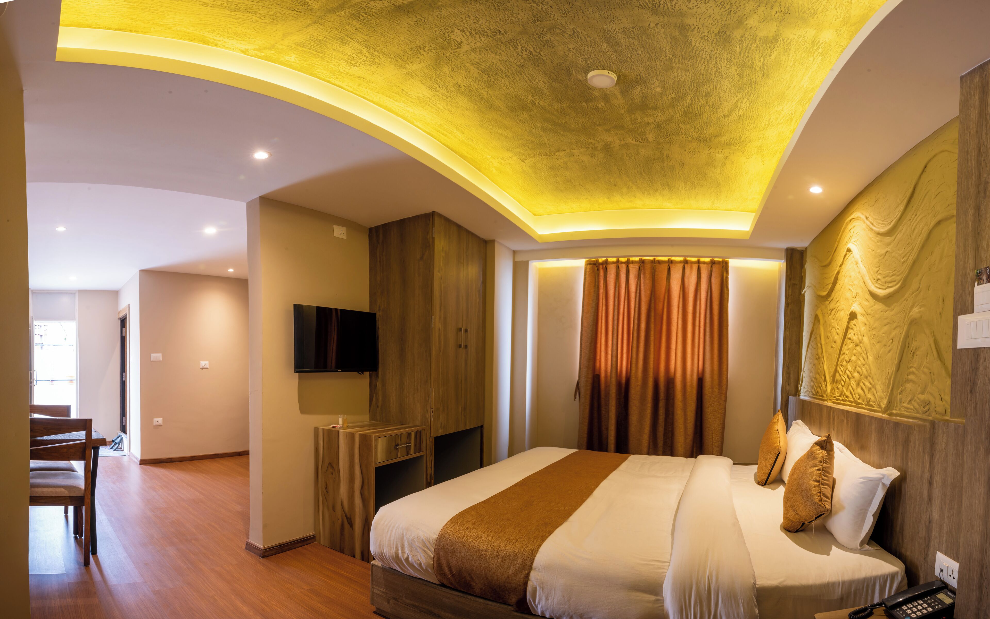 A modern hotel room with a curved ceiling, a flat-screen TV, a wooden wardrobe, a bed with white and brown bedding, and a statue on the wall.
