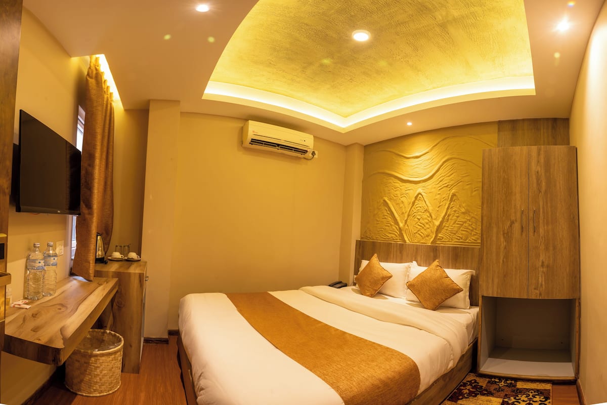 A hotel room with a bed, a wooden nightstand, a TV, and a ceiling light fixture.