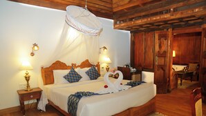 Ein hölzernes Himmelbett mit Moskitonetz, Nachttischlampen und einer Blumenkomposition.
