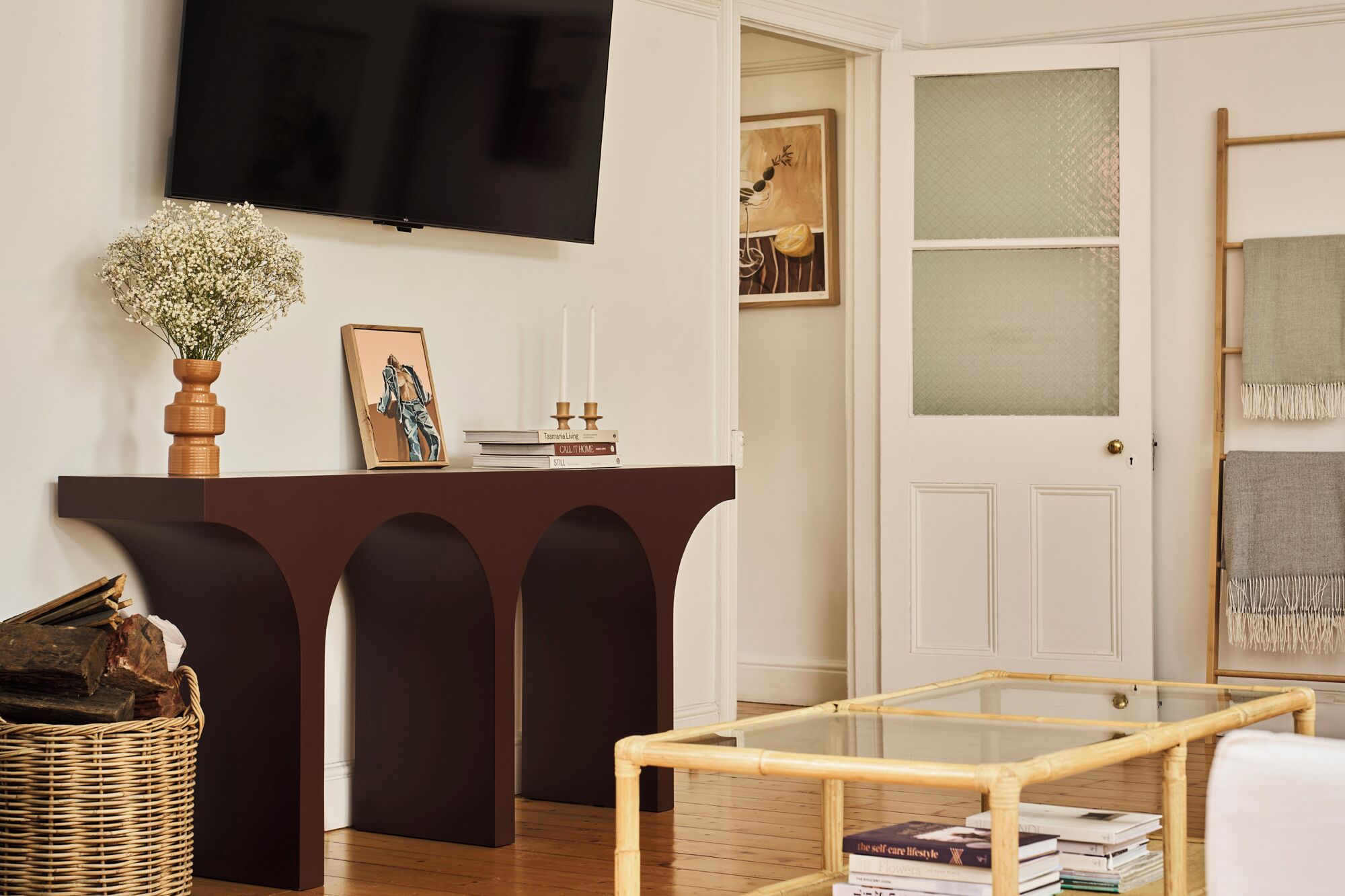 A living room with a dark brown console table, a glass coffee table, a TV mounted on the wall, and a white door with frosted glass panels.