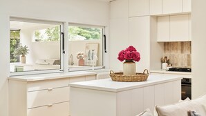 Eine moderne Küche mit weißen Schränken, einem großen Fenster und einer zentralen Kochinsel mit Korb und Blumen.