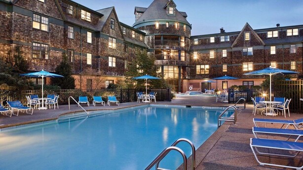 A pool area with lounge chairs and umbrellas, surrounded by a large brick building with multiple windows and a turret. - Experience Timeless Charm at Club Wyndham Long Wharf - 2 Bd. Deluxe (Newport)