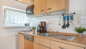 A compact kitchen with a microwave, coffee maker, and various utensils on the wall. - Cozy vacation apartment in Zinnowitz with garden, only 750 m from the beach (Zinnowitz)