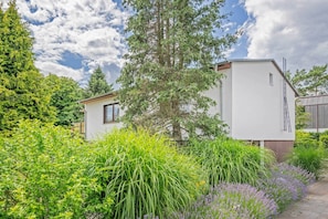 A modern white building with a flat roof, surrounded by lush greenery and a variety of plants.