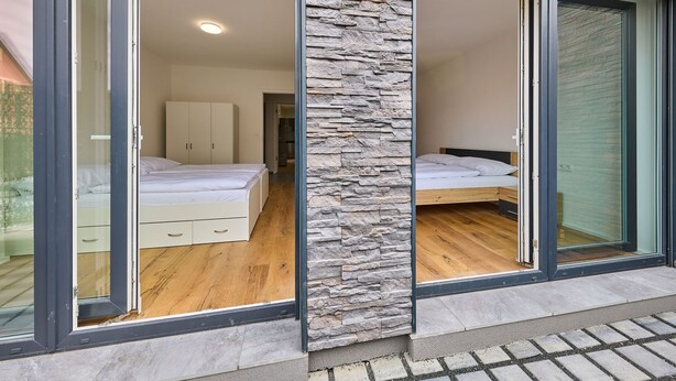 Une chambre à coucher moderne avec un mur d’accent en pierre, un plancher en bois et une grande porte-fenêtre coulissante donnant sur un balcon.