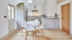 A modern kitchen with a central island, white cabinetry, and a dining area with white chairs. - Host Stay Sunshine Cottage (Leyburn)