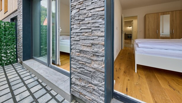 A modern bedroom with a stone facade, a large window, and a wooden floor.