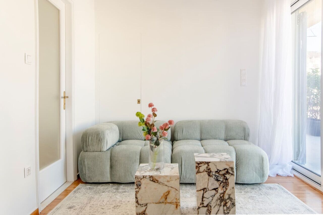 Un salon moderne avec un canapé gris, deux petites tables d’appoint en marbre et un vase de fleurs.