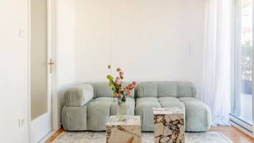 Un salon moderne avec un canapé gris, deux petites tables d’appoint en marbre et un vase de fleurs.