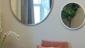 Ein rosafarbenes Sofa mit vielen Kissen, ein großer runder Spiegel und ein kleinerer Spiegel an der Wand.