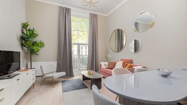 Ein modernes Wohnzimmer mit Fernseher, Sofa, Esstisch und großen Fenstern.