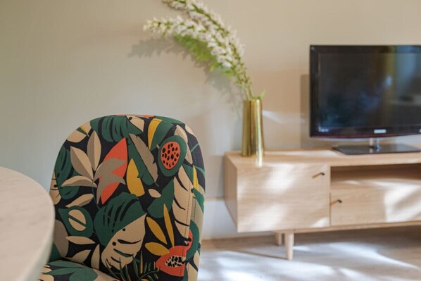 Une chambre d’hôtel avec un lit, un téléviseur posé sur une commode en bois et une plante décorative.