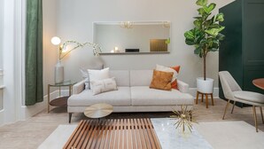 Ein modernes Wohnzimmer mit einer Couch, einem Beistelltisch, einer Lampe, einem Topf mit Pflanze und einem Sessel.