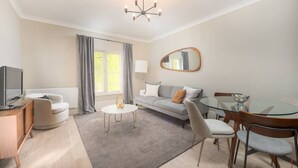 A modern living room with a sofa, a glass dining table, a TV, and a chandelier. - Gorgeous Apartment by the Park (PS6) (Greater London)