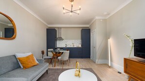 A modern living room with a grey sofa, a round white coffee table, and a dining area with a glass table and chairs. - Gorgeous Apartment by the Park (PS6) (Greater London)