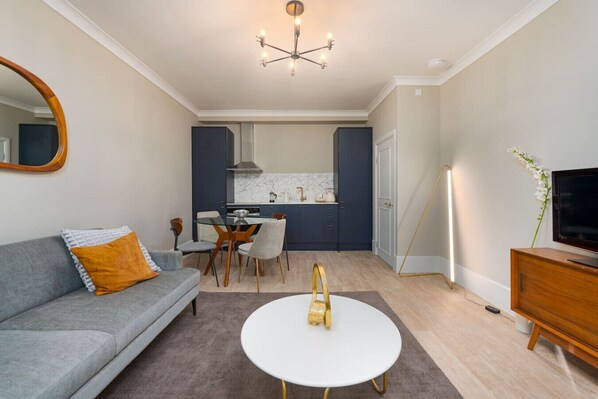 Una sala de estar moderna con un sofá gris, una mesita de centro redonda blanca y un comedor con una mesa de vidrio y sillas.