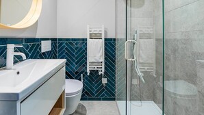 A modern bathroom with a white sink, a toilet, and a glass-enclosed shower. - Gorgeous Apartment by the Park (PS6) (Greater London)