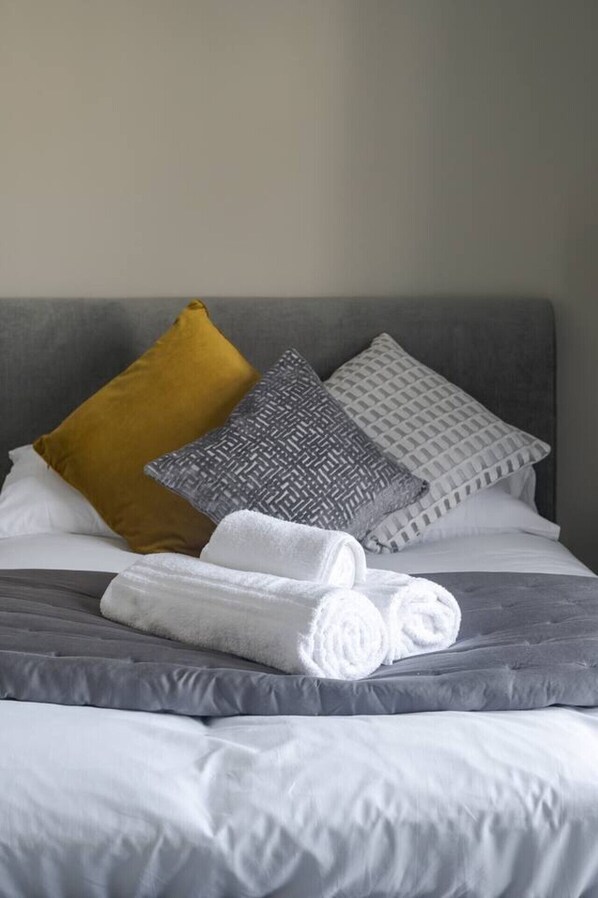 A neatly made bed with grey bedding, a yellow pillow, and patterned pillows.
