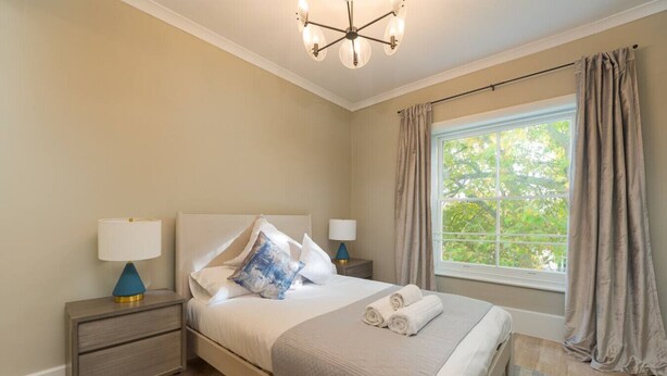A bedroom with a bed, bedside tables, a lamp, and a window with curtains. - Gorgeous Apartment by the Park (PS6) (Greater London)
