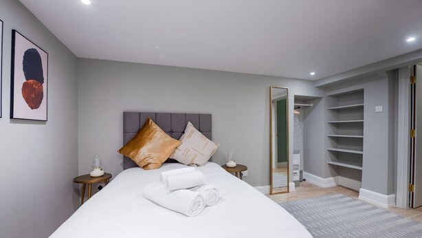 A modern bedroom with a large bed, bedside tables, a wardrobe, and a mirror. - Trendy Flat by Hyde Park (PS1) (Greater London)