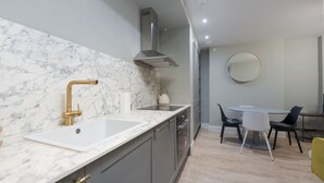 A modern kitchen with a marble countertop, a stainless steel range hood, and a dining area with a round mirror and chairs. - Trendy Flat by Hyde Park (PS1) (Greater London)