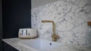 Een keuken met een marmeren aanrecht, een witte spoelbak en een messing kraan.