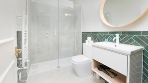 Een moderne badkamer met een douchecabine van glas, een wit wastafelmeubel met een groene tegelachtergrond en een ronde spiegel.