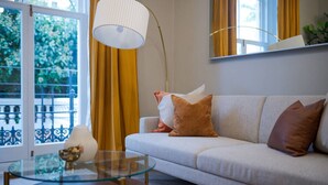 Een woonkamer met een bank, een glazen salontafel, een lamp en uitzicht door een raam met gordijnen.