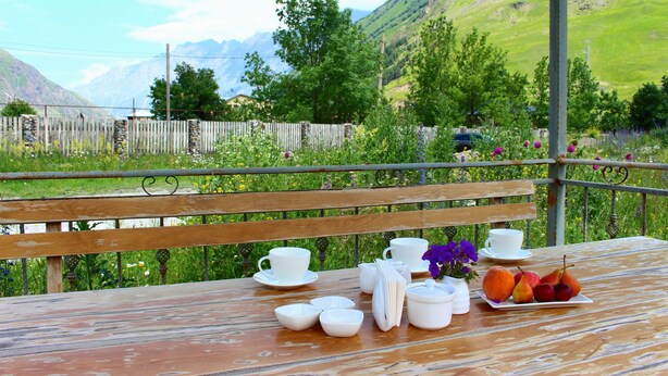 A wooden table with tea sets and fruit, set against a scenic mountain backdrop. - Hotel TWINS Achkhoti (Kazbegi)