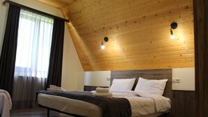 A bedroom with a sloped ceiling, wooden walls, a large bed with white and dark bedding, and two wall-mounted lights. - Hotel TWINS Achkhoti (Kazbegi)