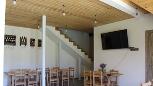 A dining area with wooden tables and chairs, a staircase, and a mounted television. - Hotel TWINS Achkhoti (Kazbegi)