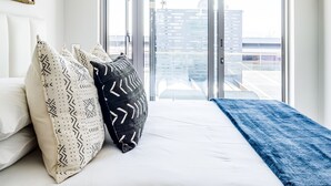 A modern bedroom with a large bed, patterned pillows, a blue throw, and a city view through floor-to-ceiling glass doors. - Deluxe Urban Retreat Summit on Quarter (Cape Town)