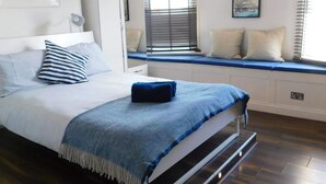 Une chambre à coucher avec un lit, un coin fenêtre aménagé en siège, un tableau encadré et une lampe fixée au mur.