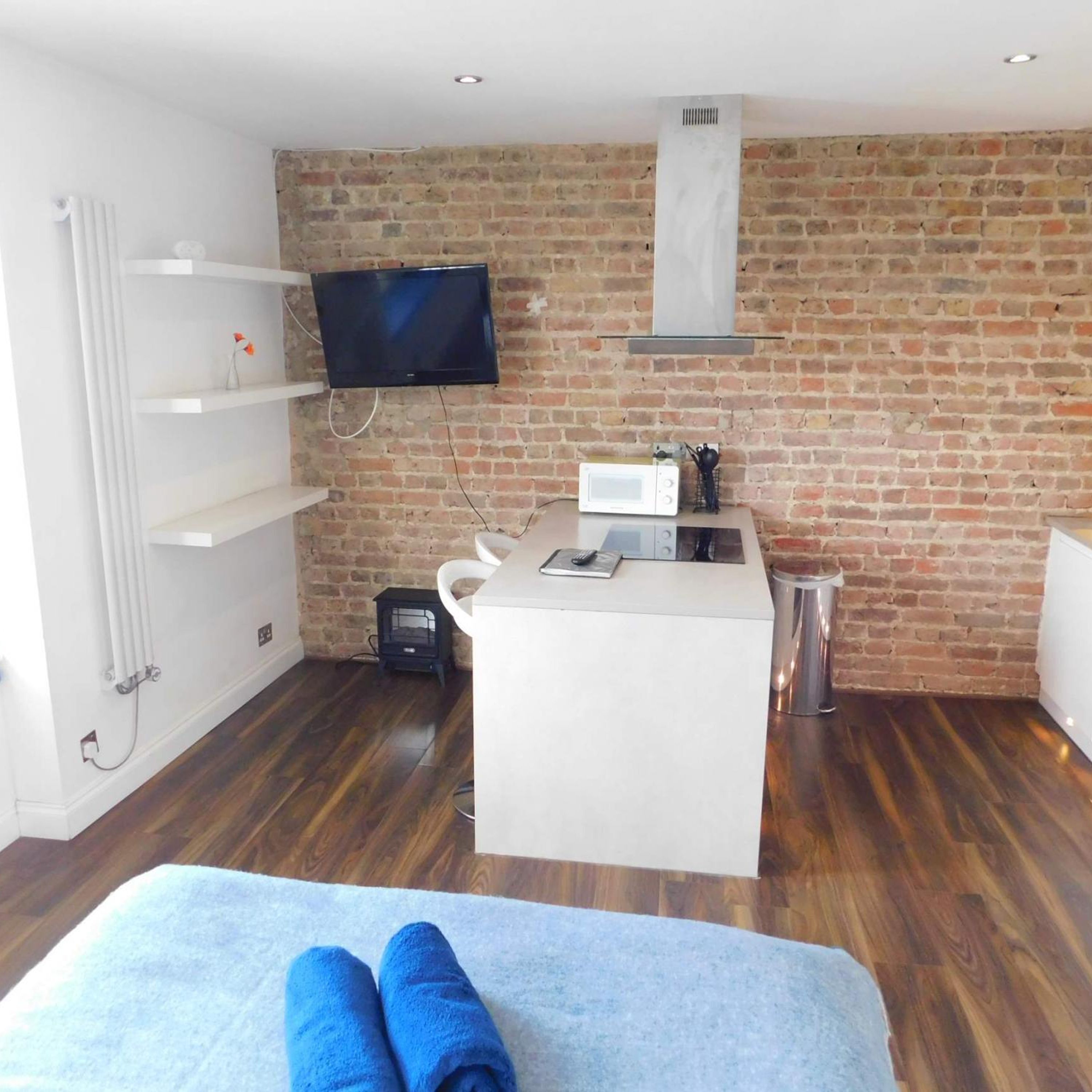 Ein modernes Zimmer mit Backsteinwand, einem flachbildfernseher über einer weißen Kücheninsel und einem kleinen schwarzen Heizgerät am Boden.