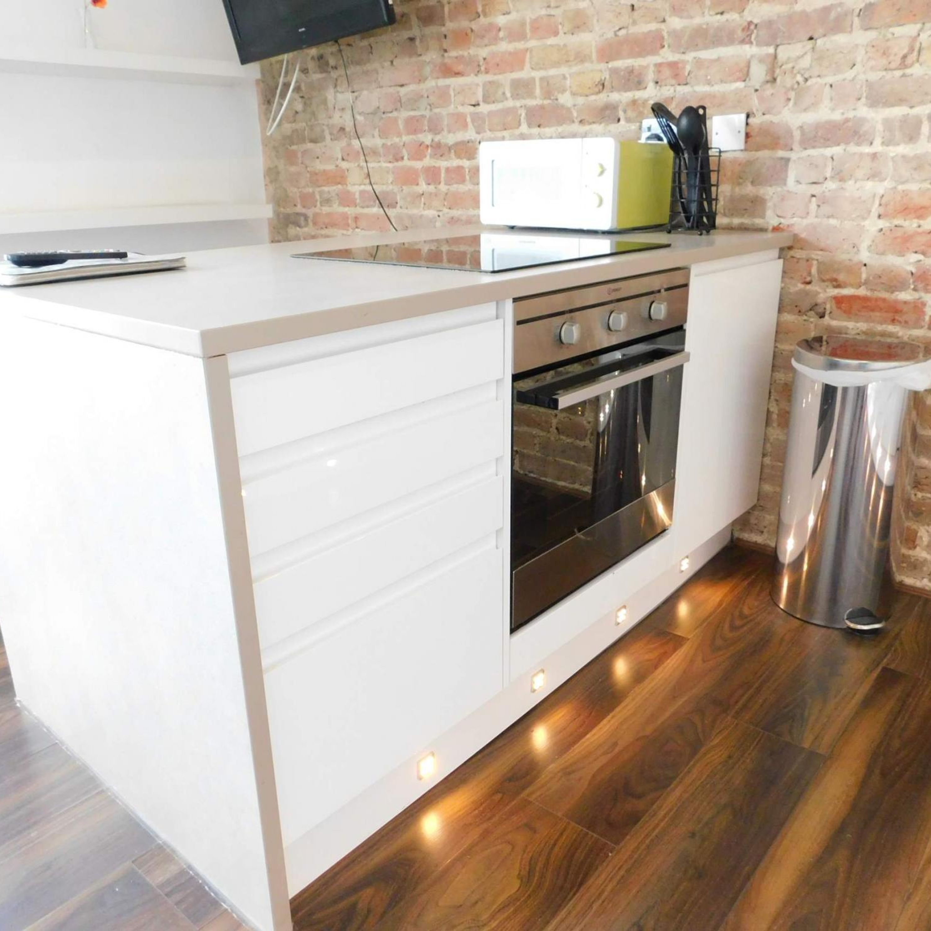 A compact kitchen with a built-in oven, a toaster, and a trash bin.