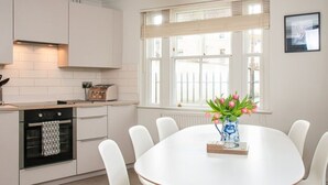 A modern kitchen with white cabinetry, a built-in oven, and a dining area with a white table and chairs.