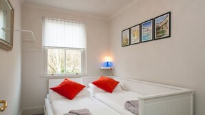A bedroom with two beds, a window with blinds, a wall-mounted lamp, and framed pictures.
