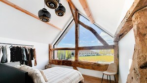 A bedroom with a large window, wooden beams, a bed, a chair, and a clothing rack. - Charming Authentic Home With Garden (Borgloon)