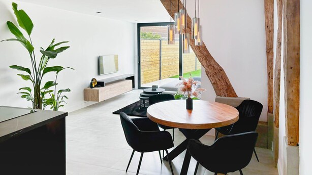 A modern dining area with a round wooden table, black chairs, and a hanging light fixture. - Charming Authentic Home With Garden (Borgloon)
